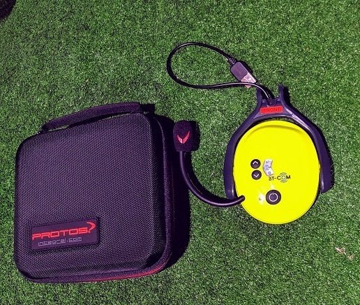 Das gelbe Protos BT COM mit Ladekabel und Verpackung auf grünem Rasen